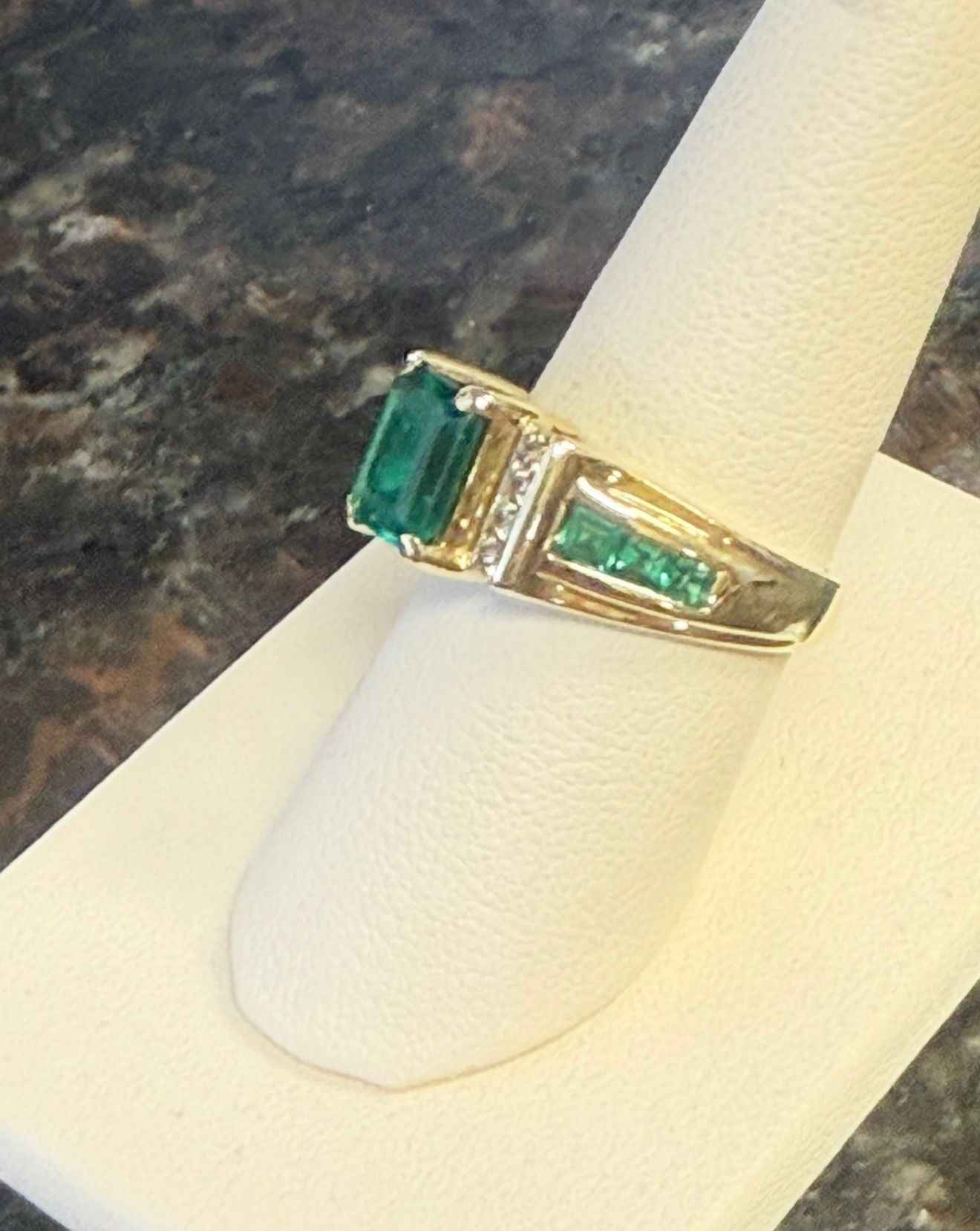 Gold ring with rectangular green gemstones displayed on a white stand