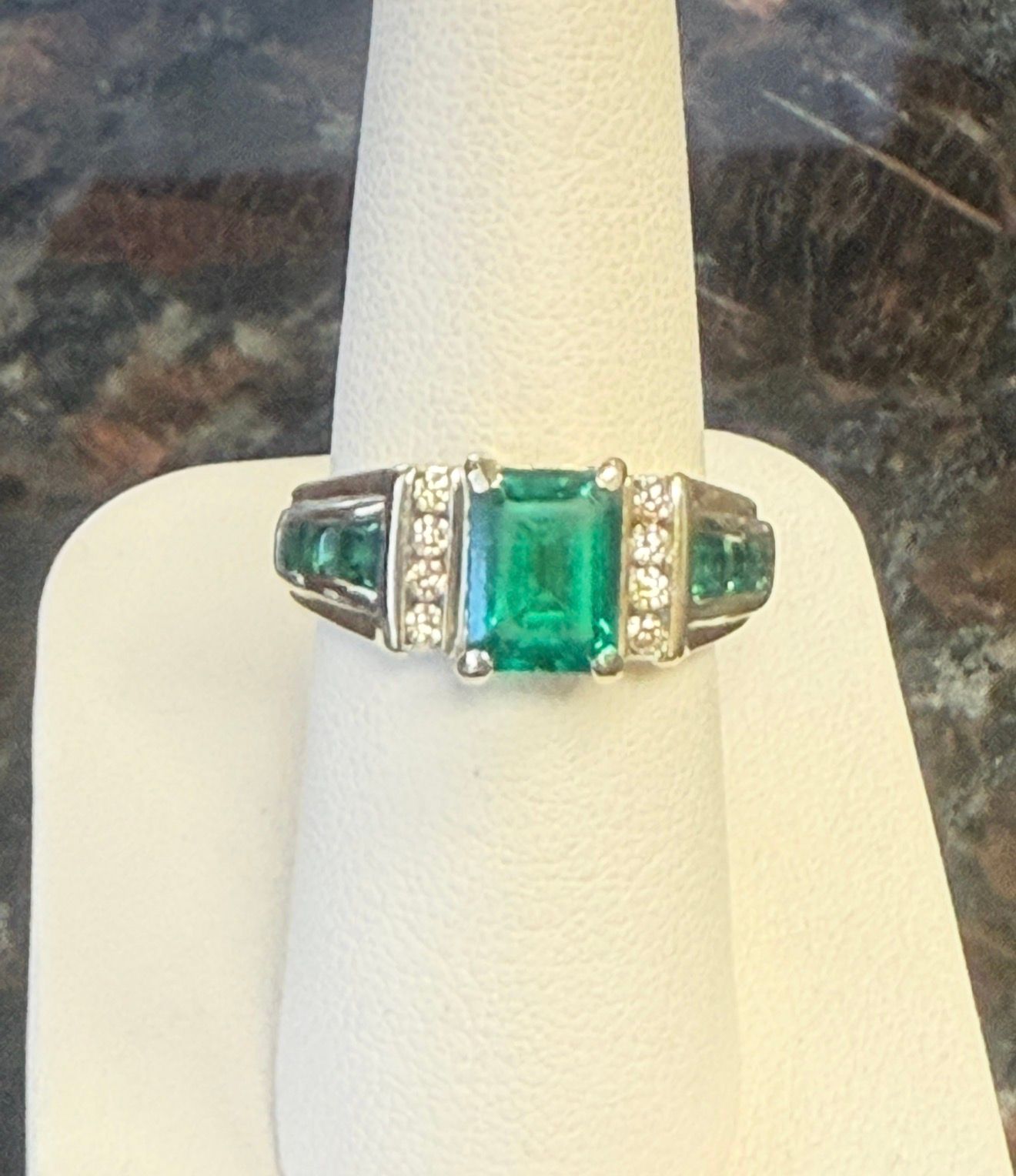 Silver ring with a rectangular green gemstone and small clear stones on a display cone