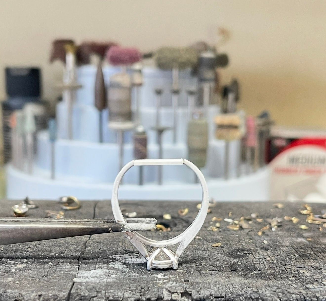 Small silver wire ring on a workbench, with blurred jewelry-making tools in the background.