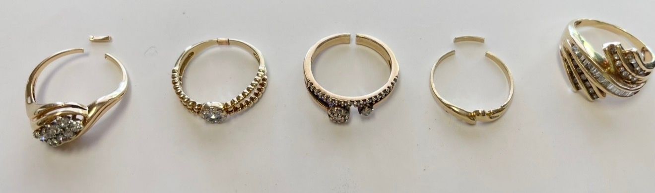 Five gold rings displayed in a row on a white background, including one larger ornate ring