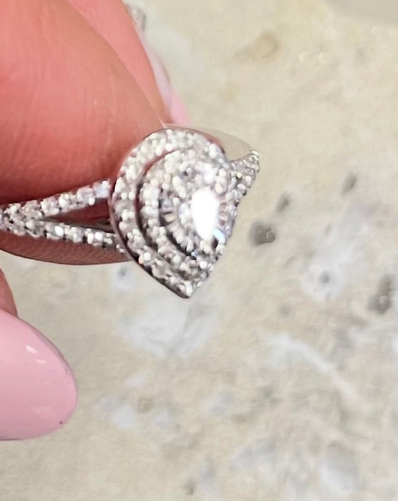 Close-up of a silver heart-shaped diamond ring held between fingers.