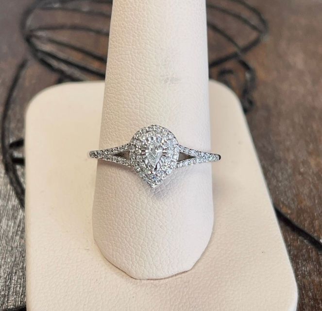 Diamond halo engagement ring on a white display stand with pavé band