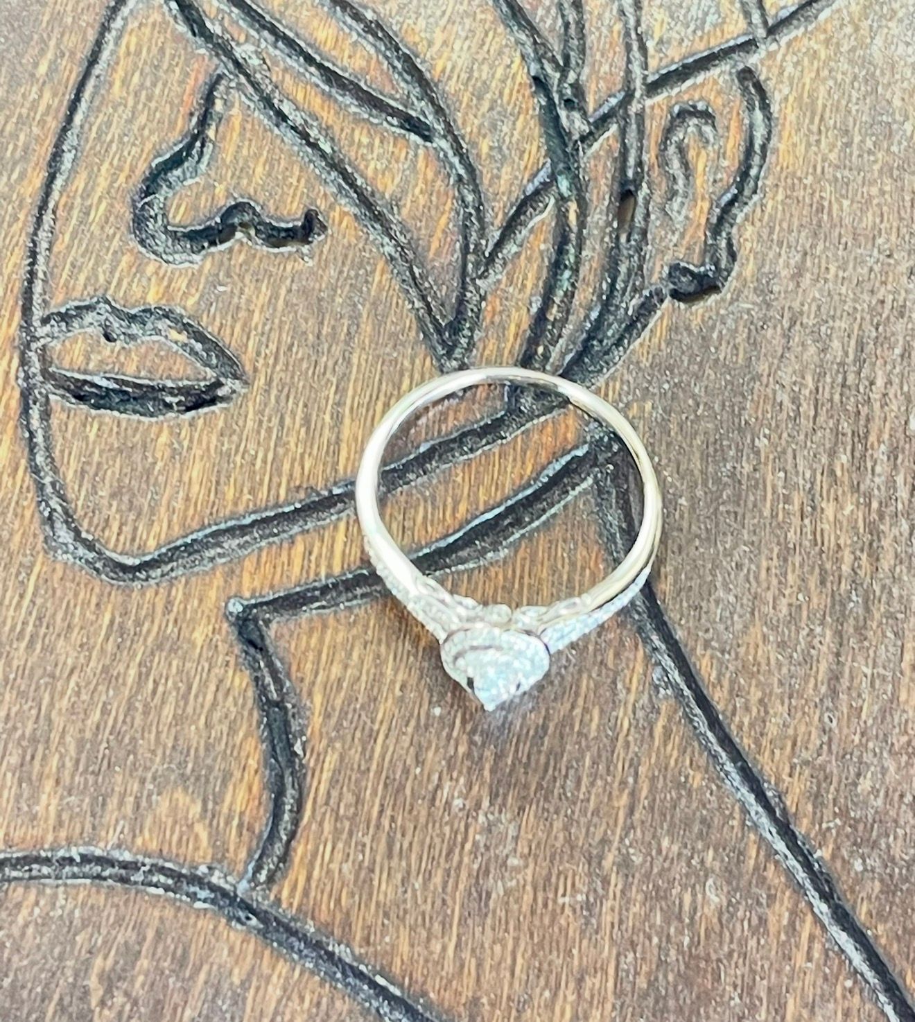 Silver ring with a heart-shaped stone on a pencil sketch of a woman’s face and neck