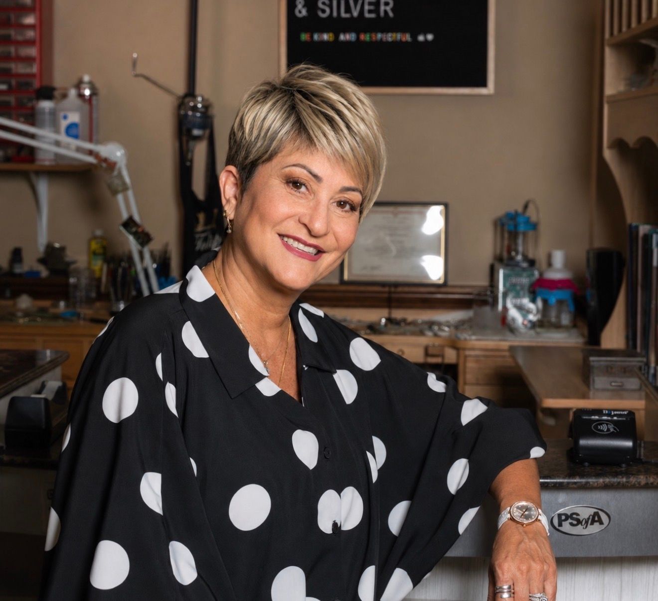 Smiling woman in a black-and-white polka dot top seated at a salon workstation