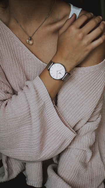 Close-up of a person wearing a pink knit sweater, silver watch, and necklace, with one hand resting on the shoulder
