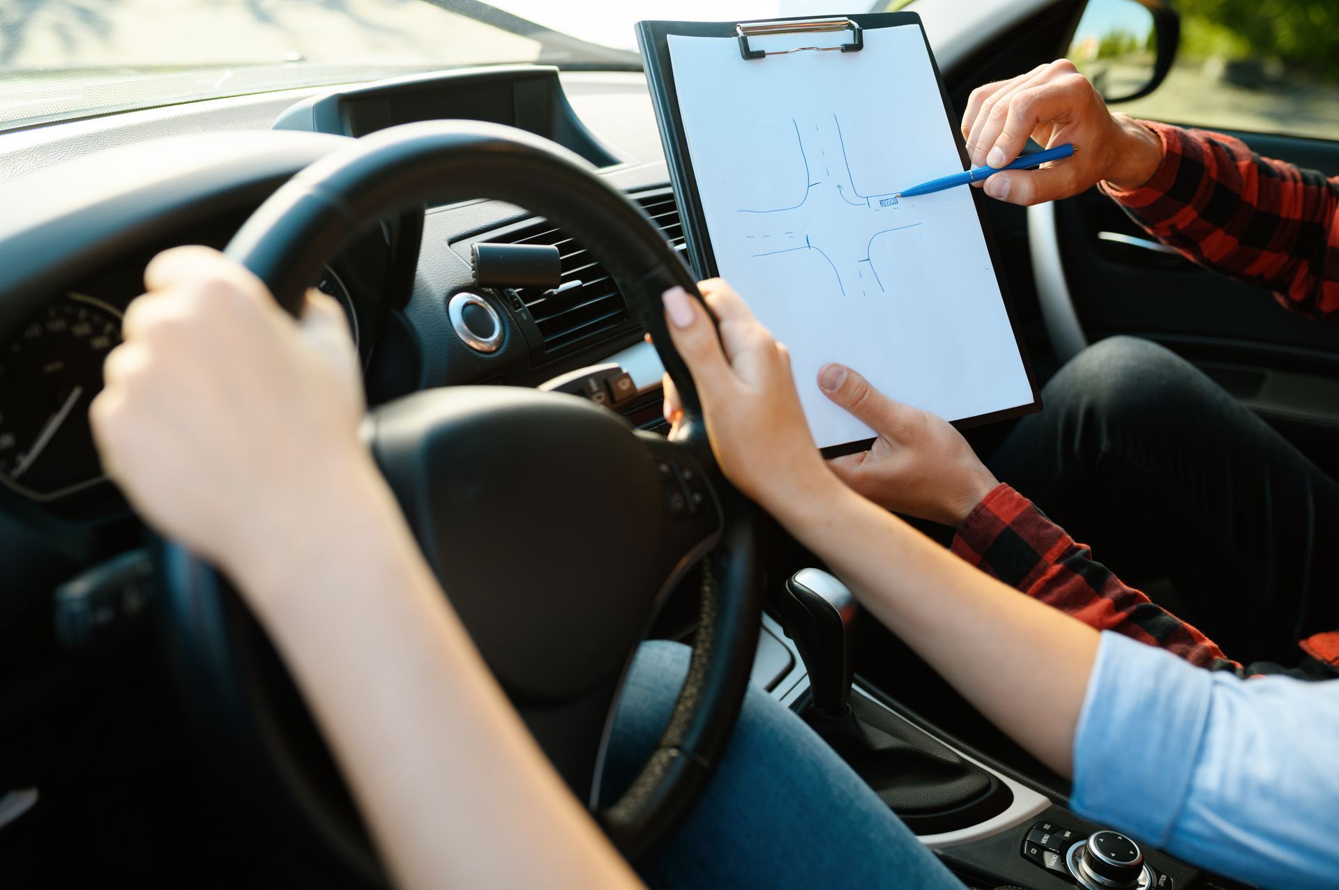 Driving instructor shows student an intersection diagram on a clipboard in a car.