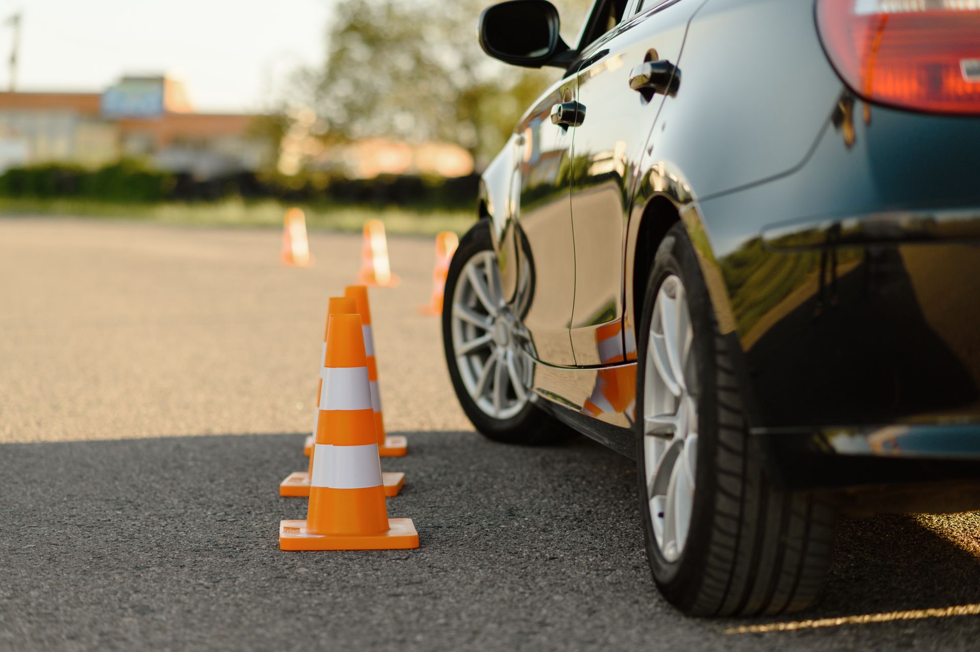 Black car beside orange traffic cone on a road, low-angle view