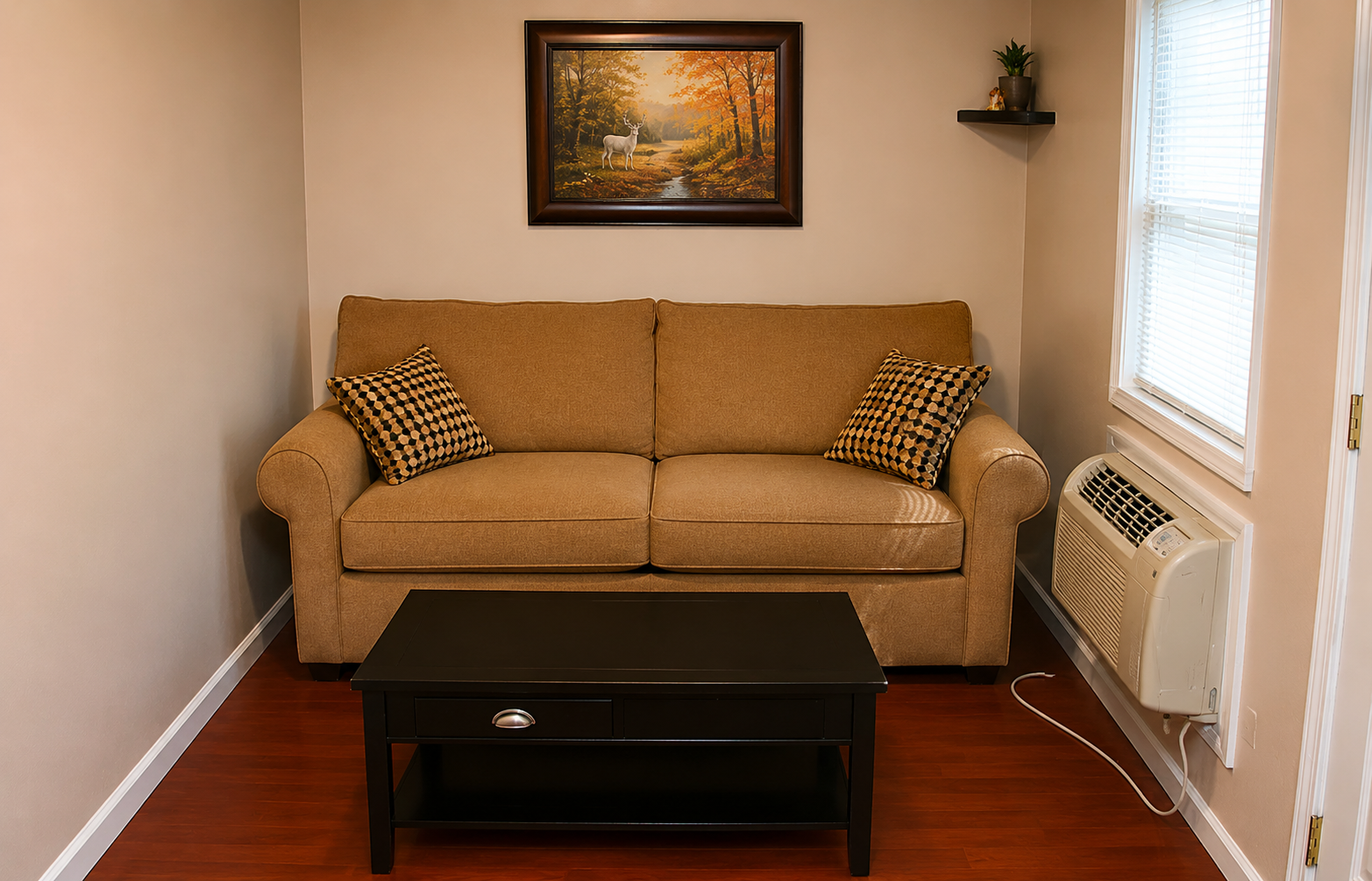 Small living room with tan sofa, black coffee table, framed wall art, and window air conditioner.