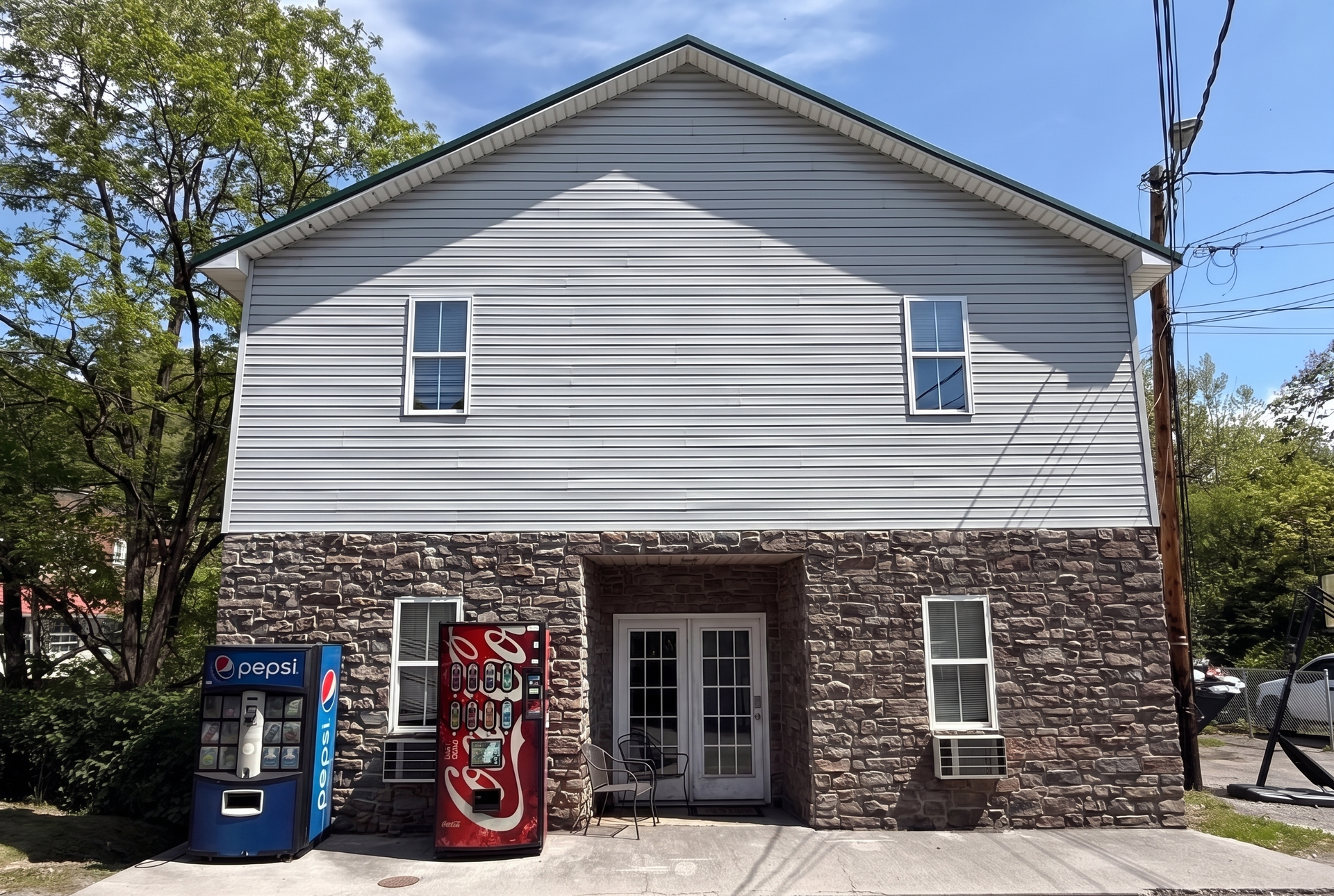 Small building with stone lower facade, white upper siding, and two vending machines by the entrance.