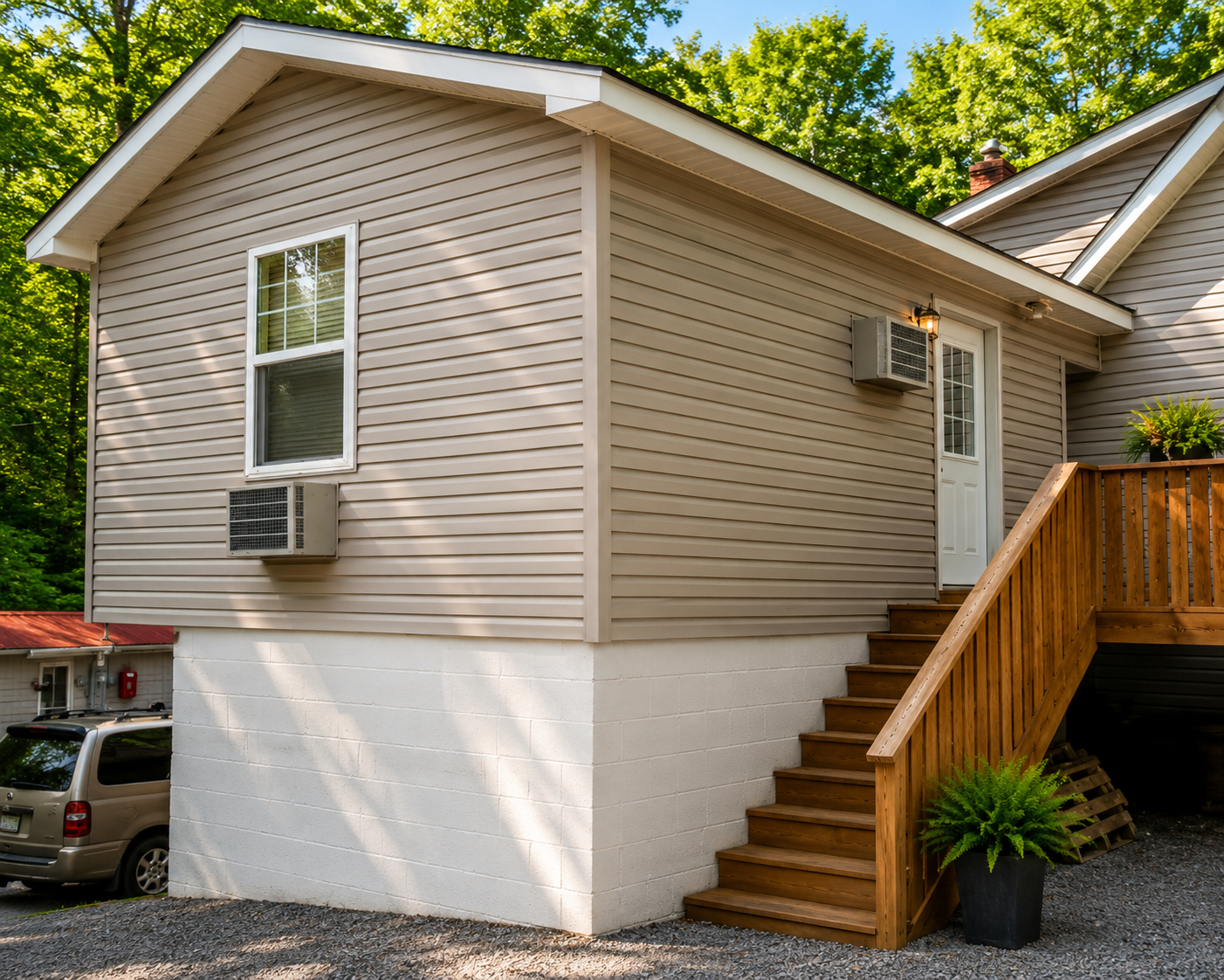 Exterior of a beige house with stairs, white foundation, and a deck beside a gravel driveway