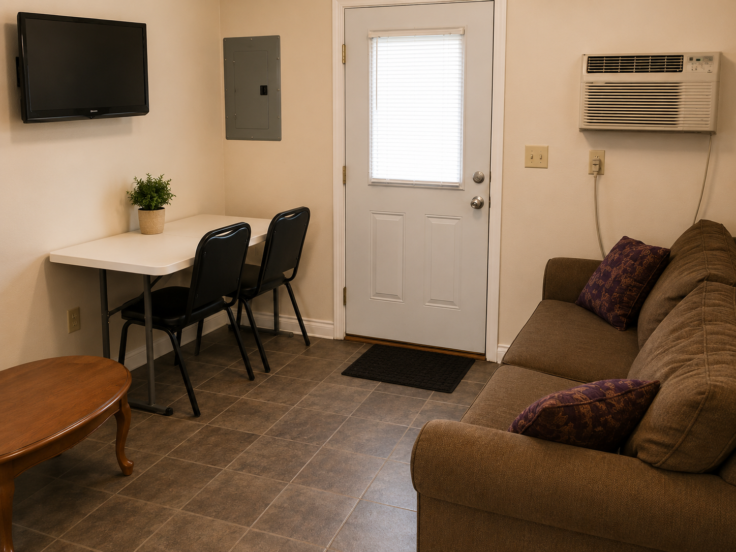 Small living room with wall TV, desk and chairs, sofa, and a door with blinds.