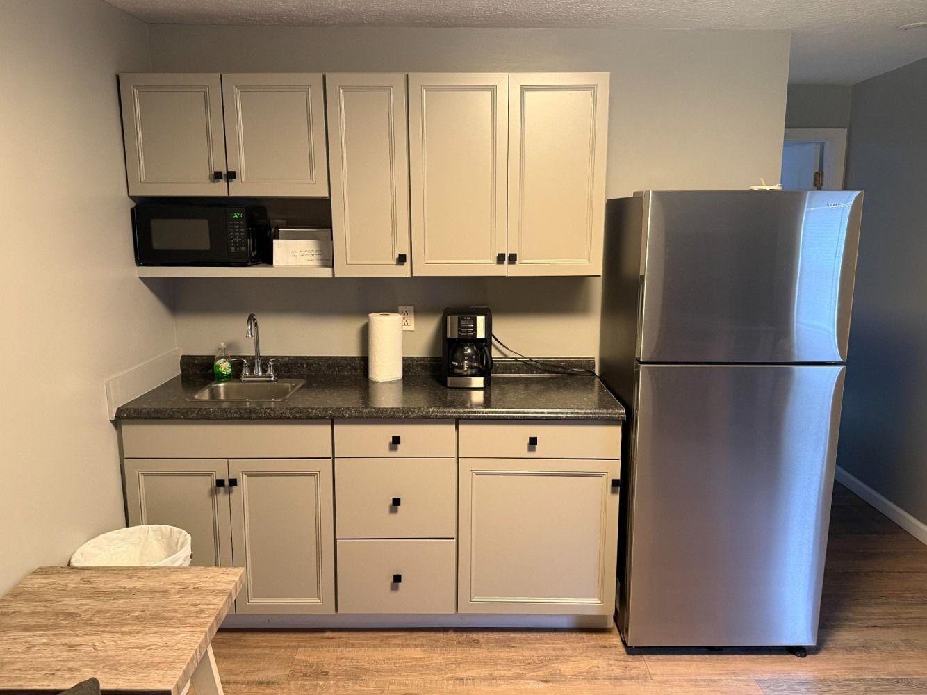Small kitchen with beige cabinets, dark countertop, stainless fridge, and coffee maker.