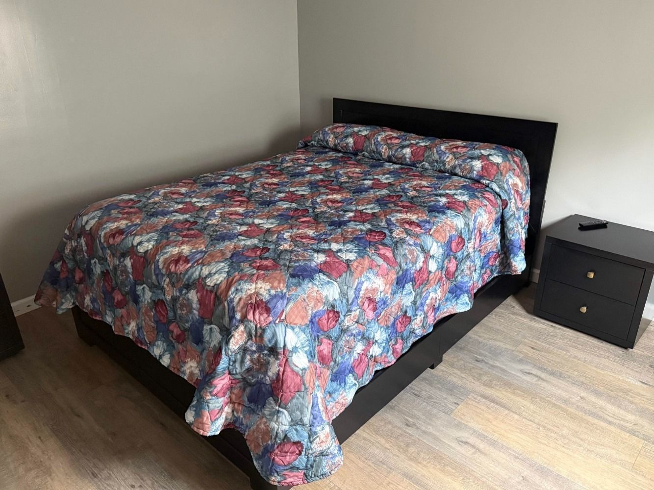 Bed with colorful patterned comforter beside a black nightstand in a simple bedroom