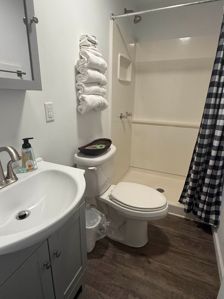 Small bathroom with sink, toilet, shower curtain, and white towels stacked on the wall.