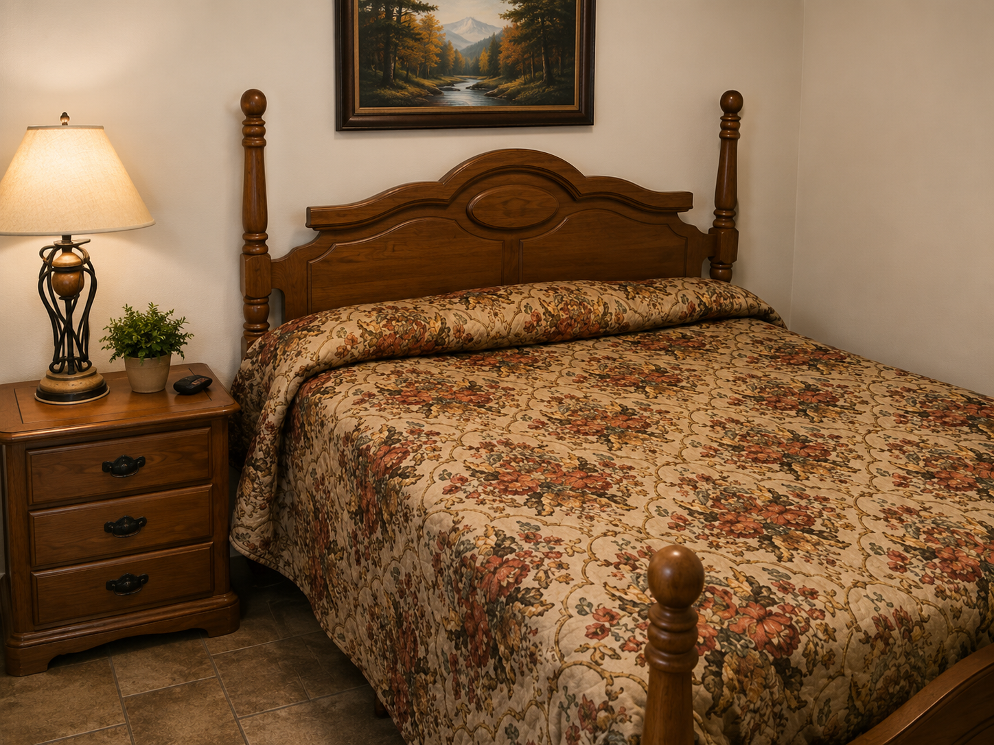 Cozy bedroom with a carved wooden bed, floral bedspread, nightstand lamp, and framed wall art.