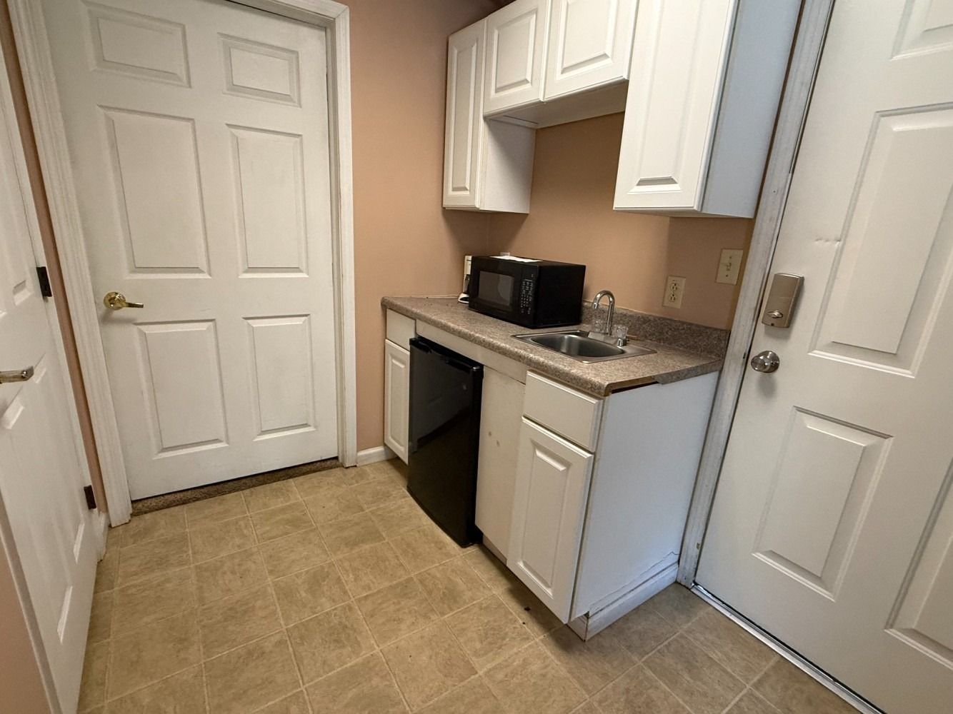 Small kitchen with white cabinets, granite counter, microwave, and tile floor beside a door.