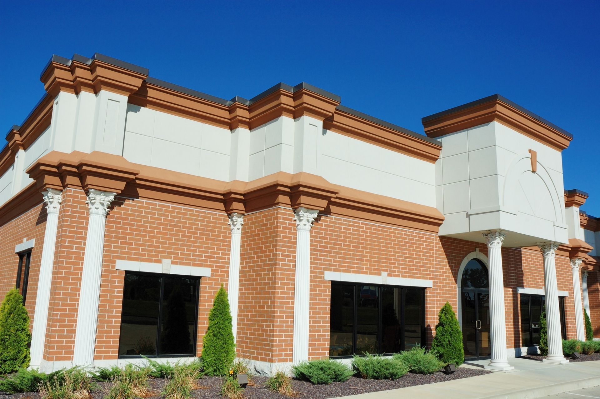 Brick storefront building with white trim, black awnings, and a covered entrance under a blue sky