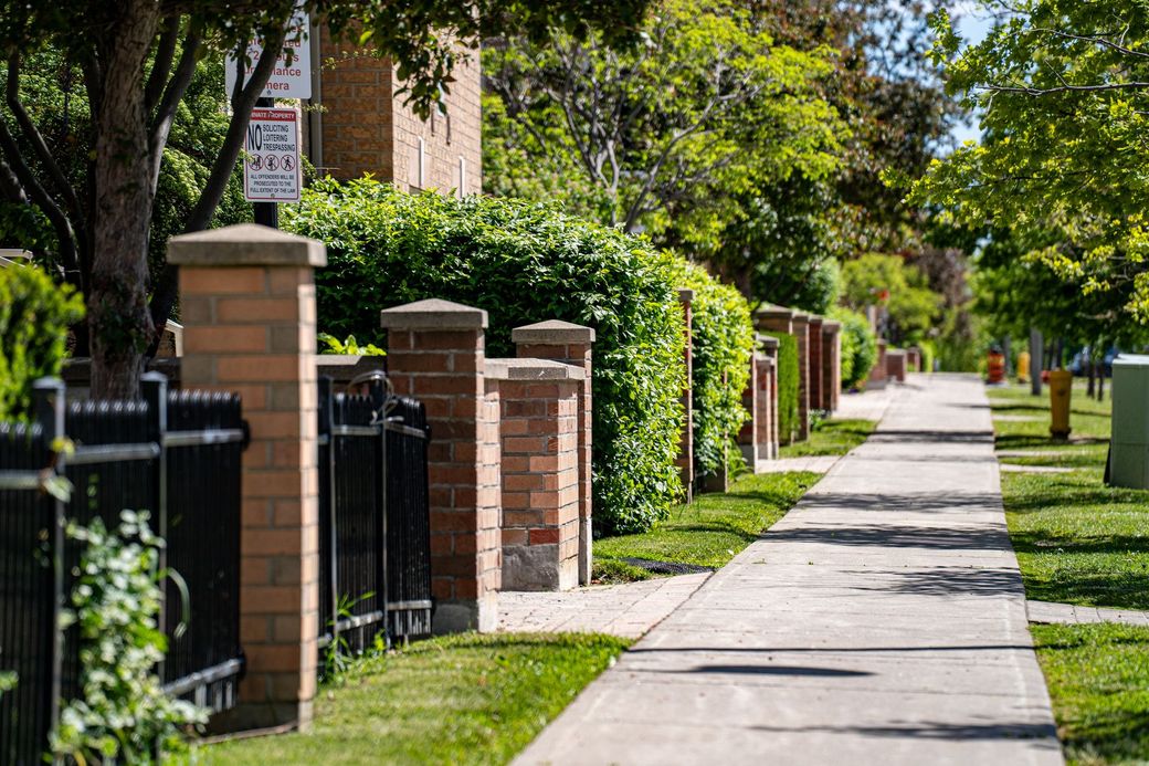 Tree-lined sidewalk beside brick-and-iron fences in a quiet residential neighborhood