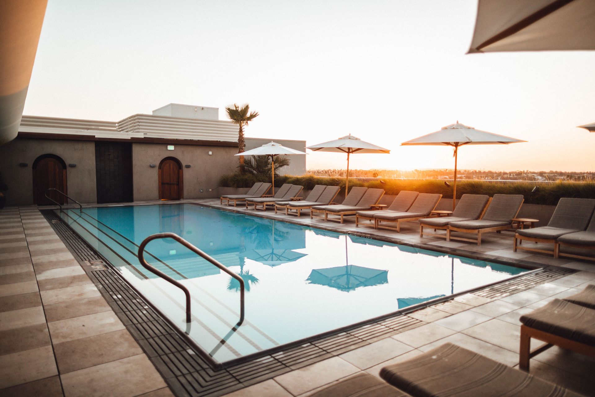 Terraço moderno de restaurante ao ar livre junto a uma piscina iluminada à noite, com mesas, cadeiras e vasos de plantas.