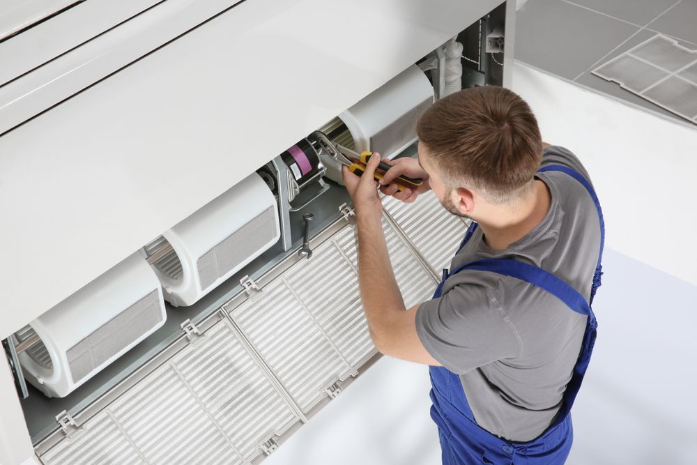 A Man Is Working On An Air Conditioner In A Room — South Coast Refrigeration & Air Conditioning In Bomaderry, NSW