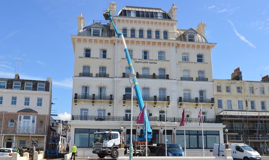 Cherry picker lifting commercial window cleaner near glass of Brighton mercure hotel