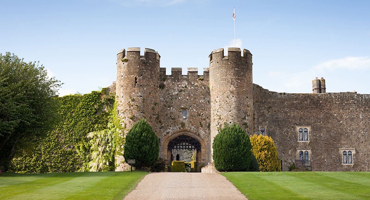 Stone castle gatehouse with two towers, doorway, green lawn and blue sky.