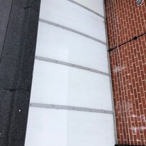 White panels on a building's wall, next to a brick wall. Black asphalt to the left.