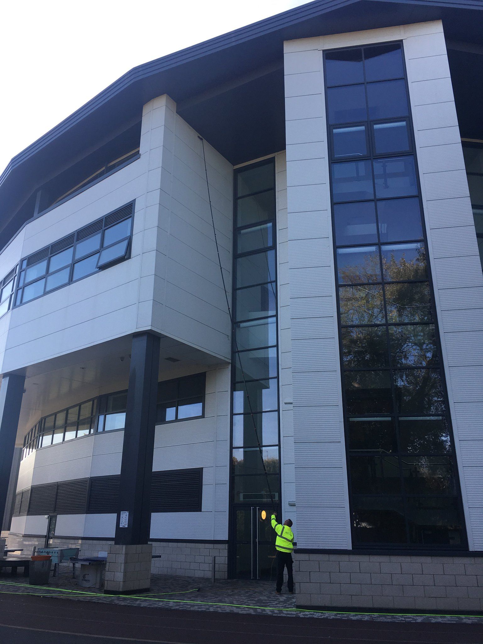 Modern office building, person in yellow vest points at doorway. White, gray, and black color scheme.