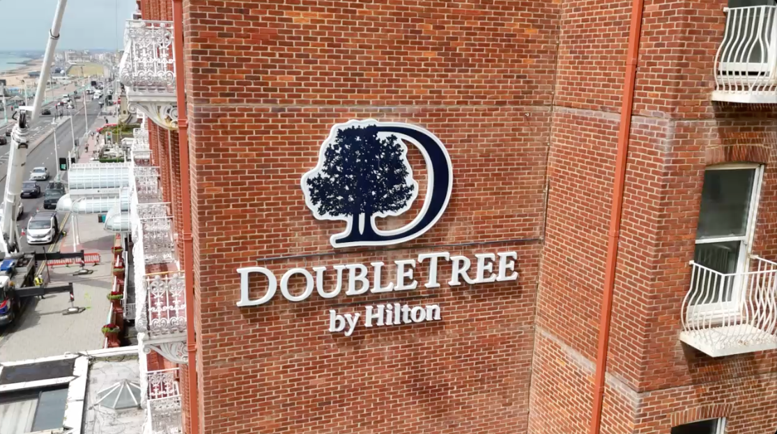 DoubleTree by Hilton hotel sign on a brick building exterior, side view before window cleaning