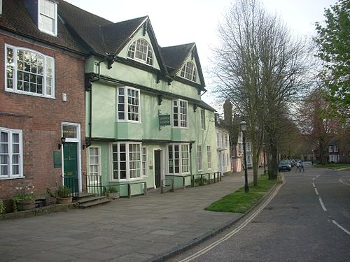 Row of colorful historic buildings along a street; green and brick facades with white-framed windows.