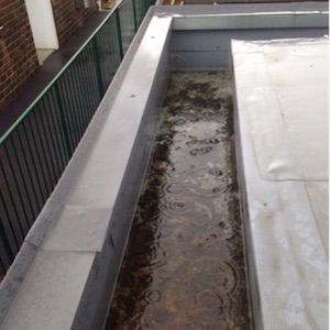 A long, rectangular roof gutter filled with rainwater, viewed from above.