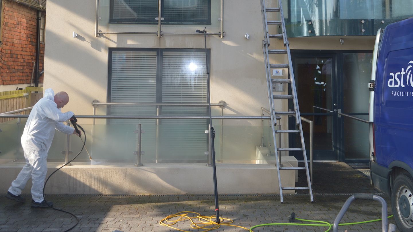Exterior cleaning specialist in full protective suit cleaning the outside of a building with pressur