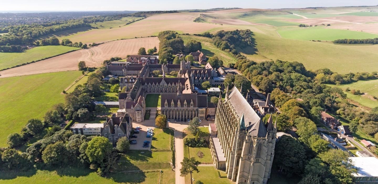 Aerial view of a large Gothic-style building complex surrounded by greenery and fields.