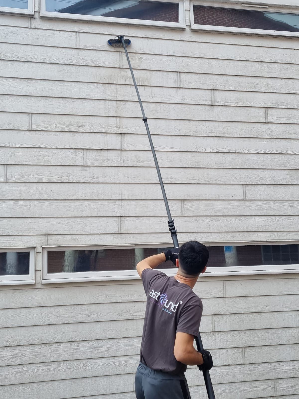 Person cleaning windows on a building using an extending pole.