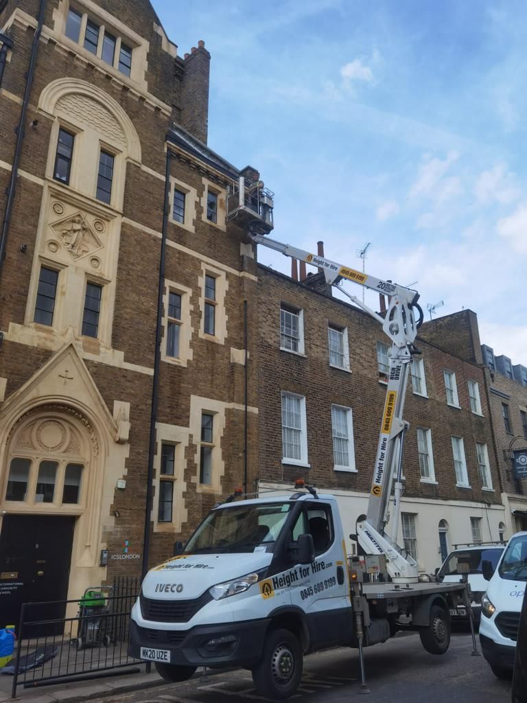 A white truck with an extended boom lift reaches a brick building for repairs.