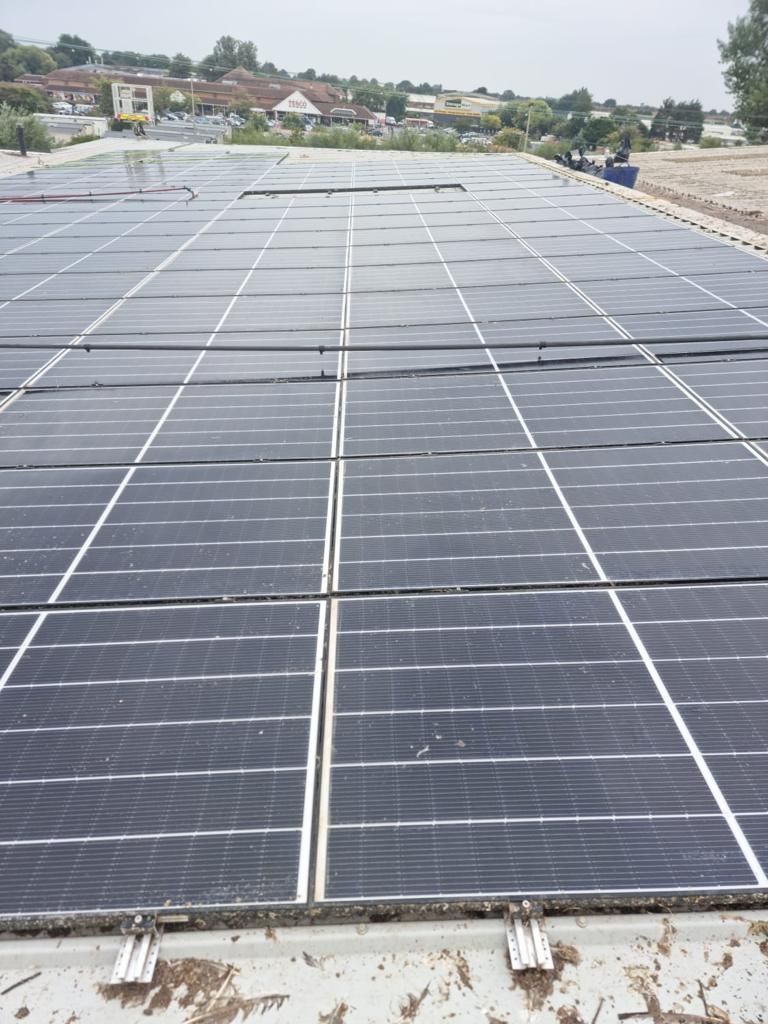 Solar panels on a rooftop, angled view. Rows of black panels with white lines, outdoors, cloudy sky.