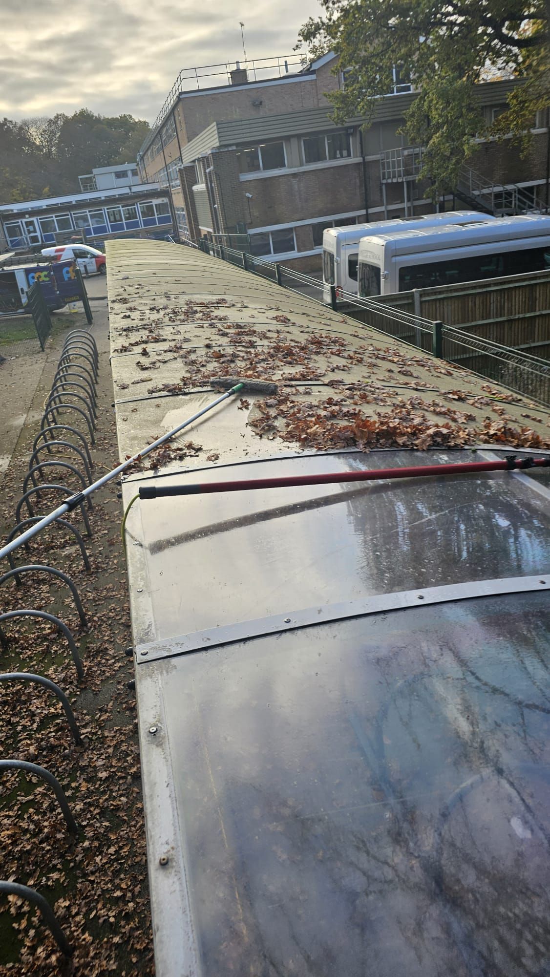 Rooftop covered in fallen leaves, a long handled tool visible. Building and parked cars in the background.