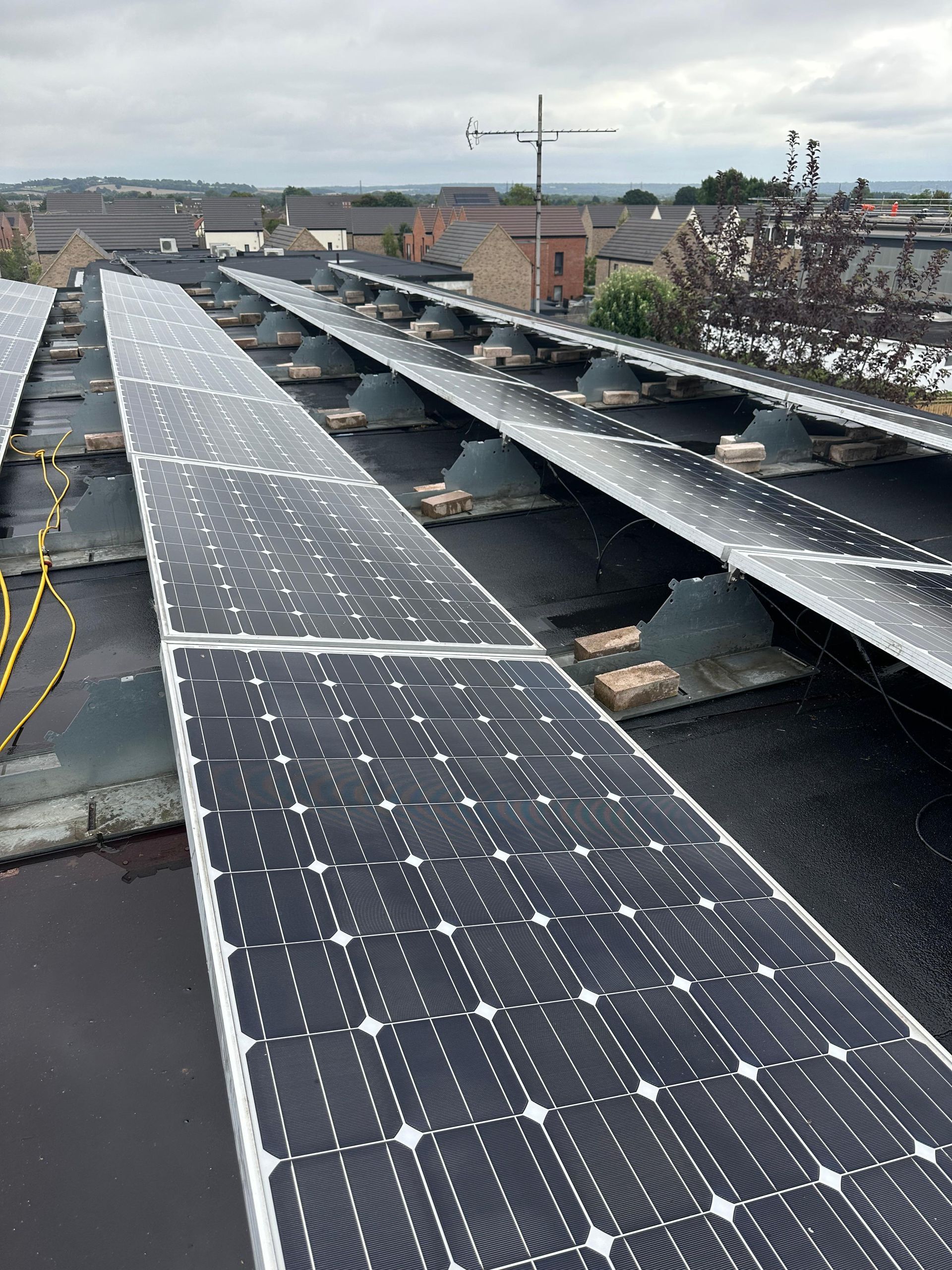 Solar panels on a flat roof with a cityscape in the background under an overcast sky.