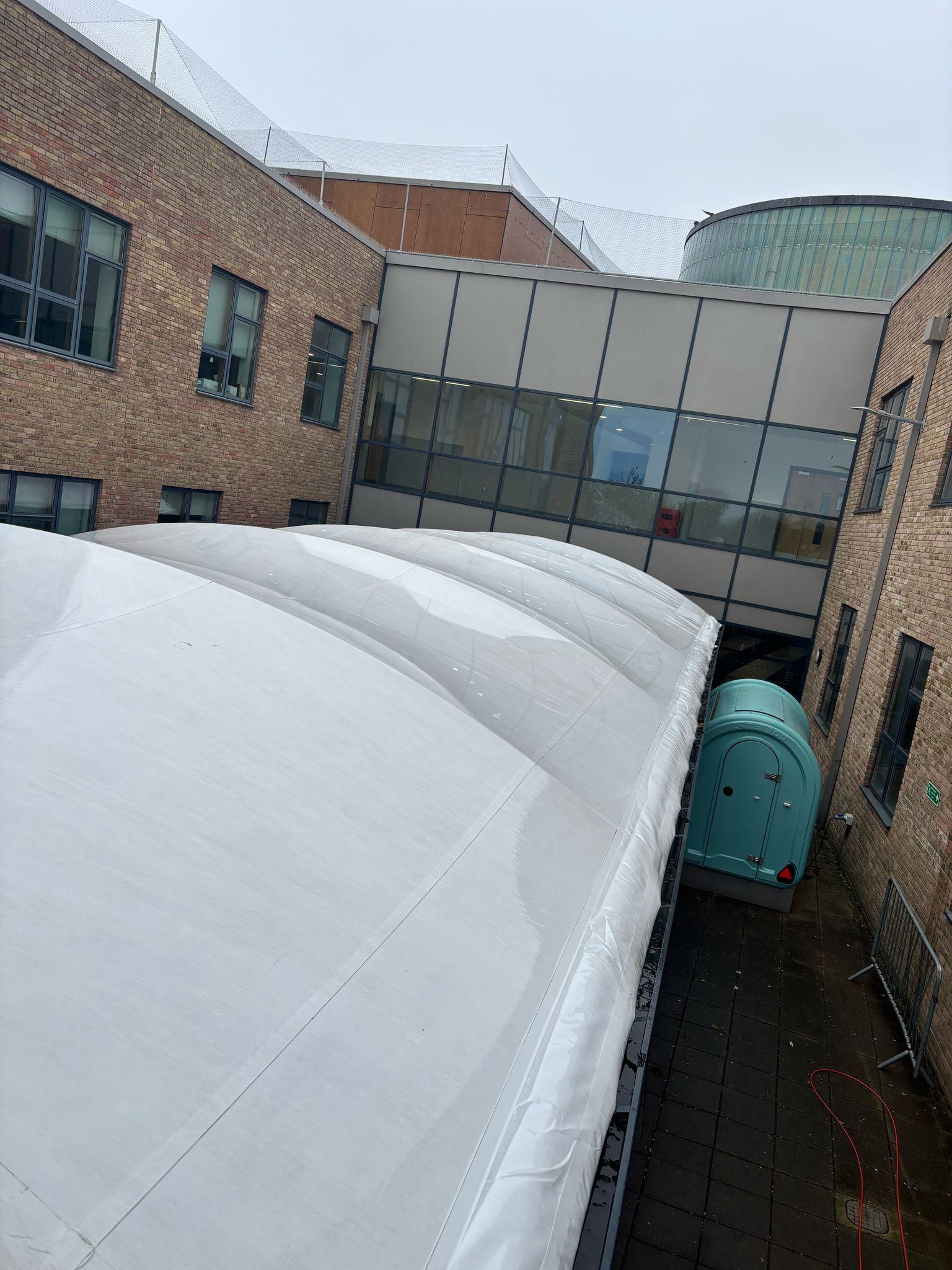 White canopy over pathway between brick buildings, a walkway connects the buildings.