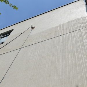 Light grey rendered facade with water streaking and algae before soft wash render cleaning