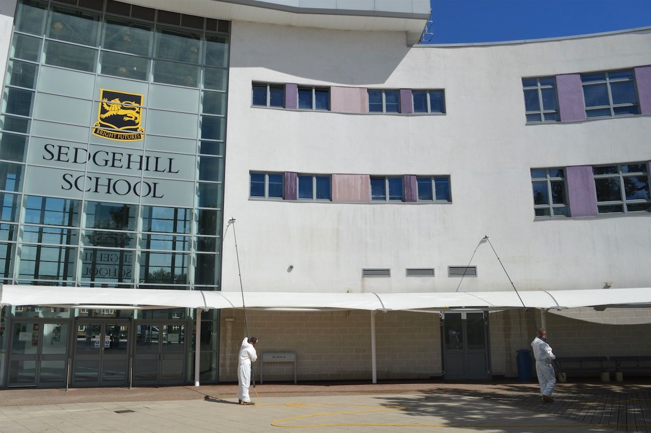 Exterior view of the Setchehill School building. Two workers in white suits spray the building's exterior with a disinfectant.