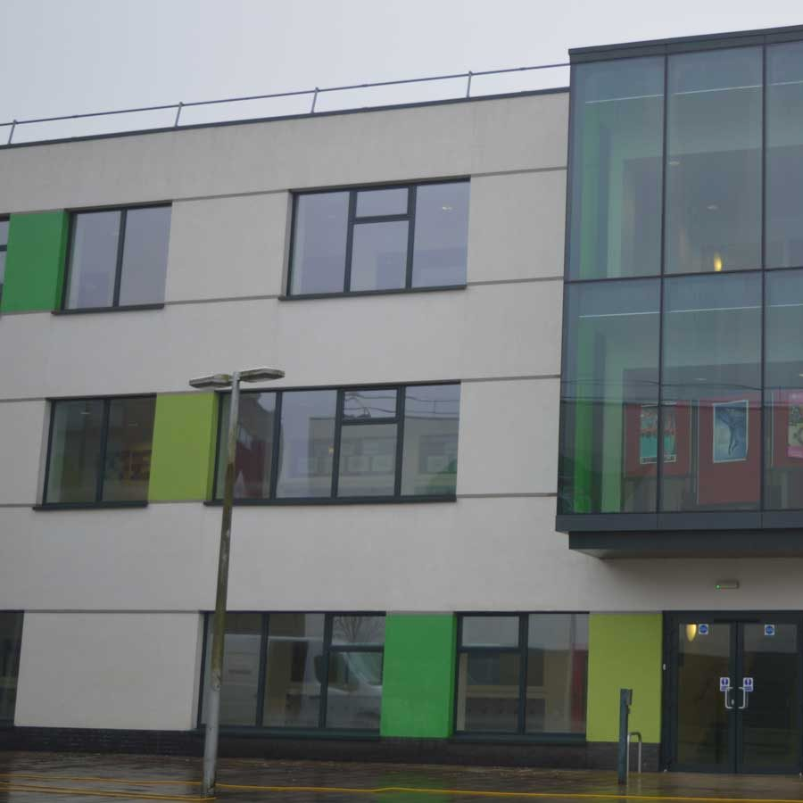 Exterior of a modern building with a glass-walled section, white walls, green accents, and multiple windows.