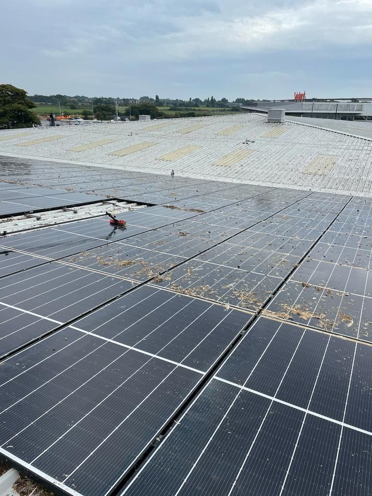 Solar panels on a commercial roof with distant buildings and a cloudy sky.