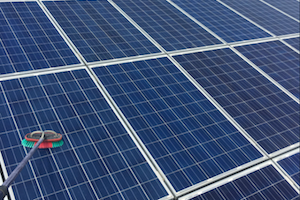 Solar panels being cleaned with a brush. Blue and white panels, clear sky.