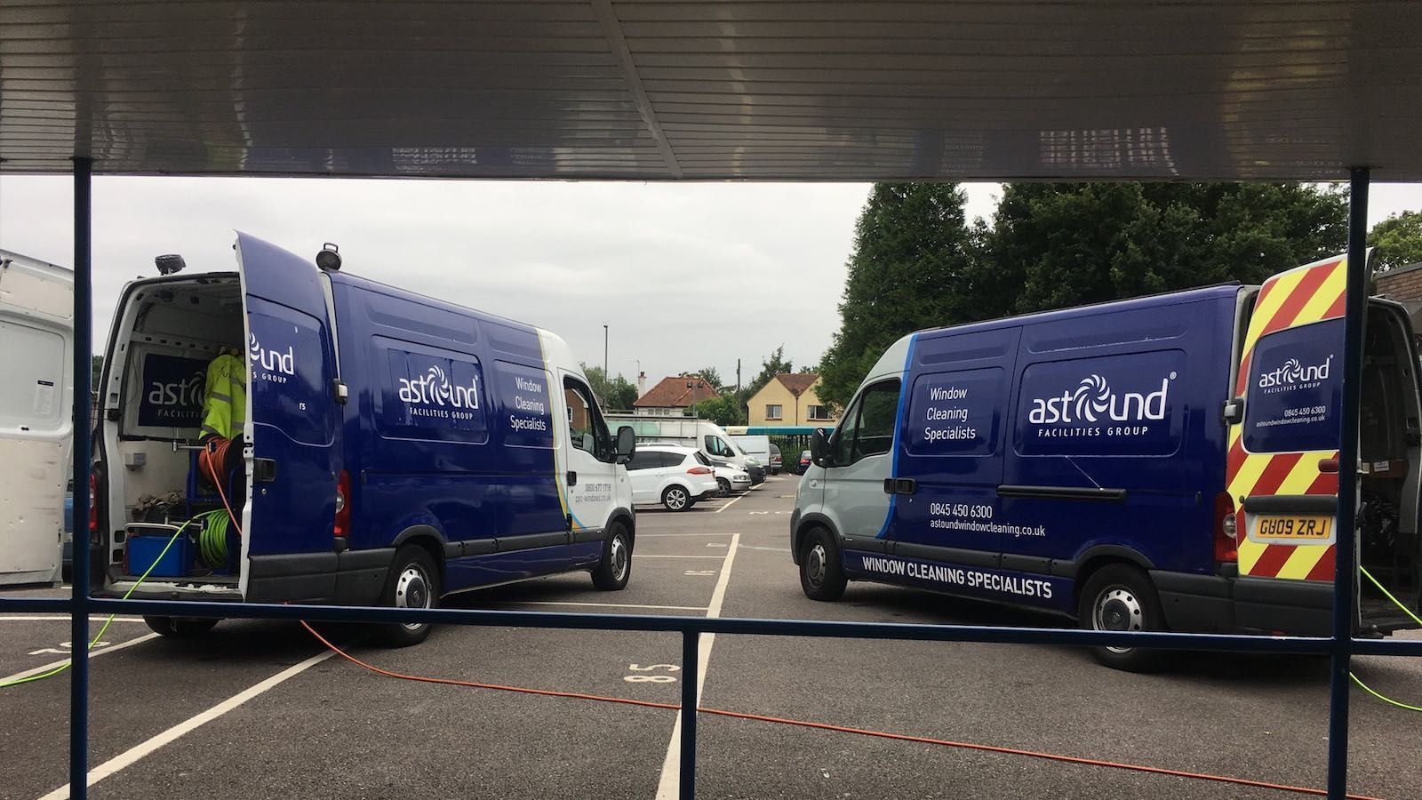 Two blue and white vans parked, doors open, in a parking lot. They have company logos.