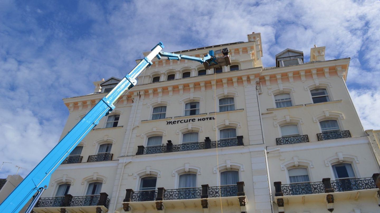 A blue lift crane working on the roof of a seafront hotel building having expert window cleaning