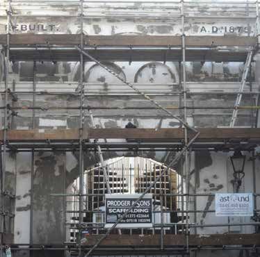 Scaffolding on a building with an arched doorway, the year 1875 is visible.
