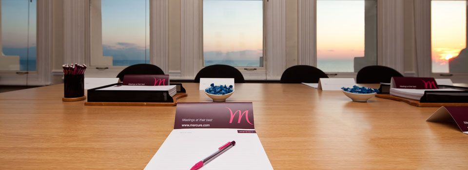 Conference room with a wooden table, chairs, and a view of the ocean and sky.