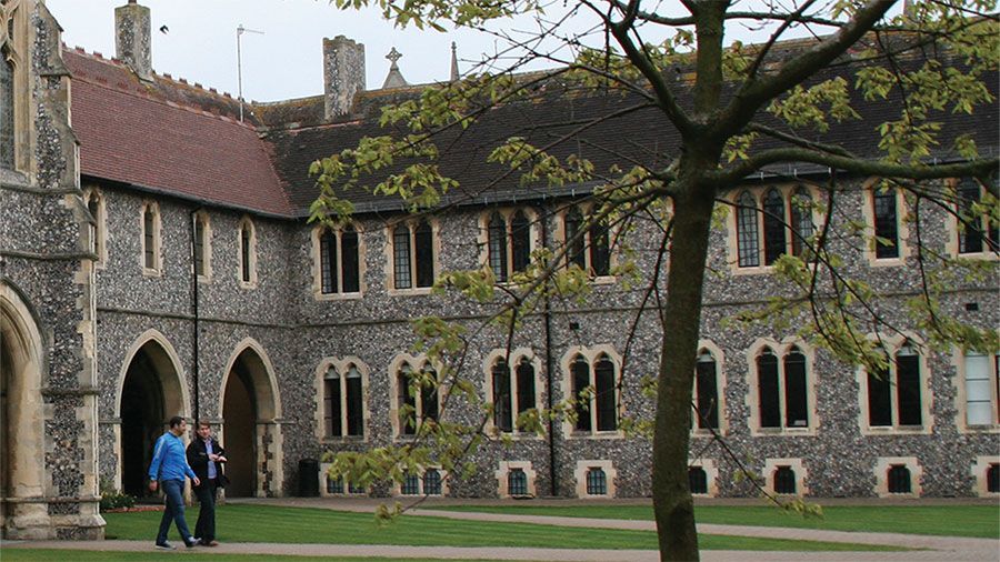 Heritage Stone buildings with arched entrances and tall windows. Two people walk in courtyard.