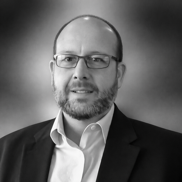Man with a beard and glasses wearing a suit jacket and dress shirt, smiling.